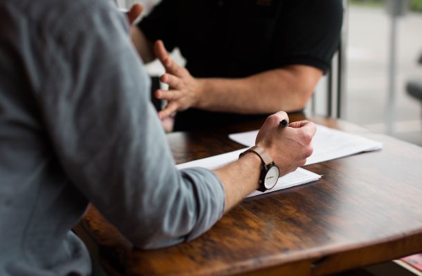 Zwei Personen im Gespräch über Dokumente bei einem Beratungstermin am Holztisch
